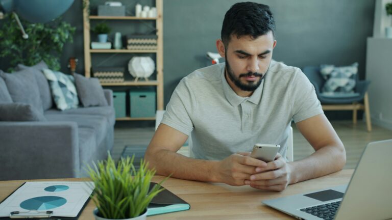 Personne utilisant un smartphone devant un ordinateur portable, illustration des agents IA mobiles.